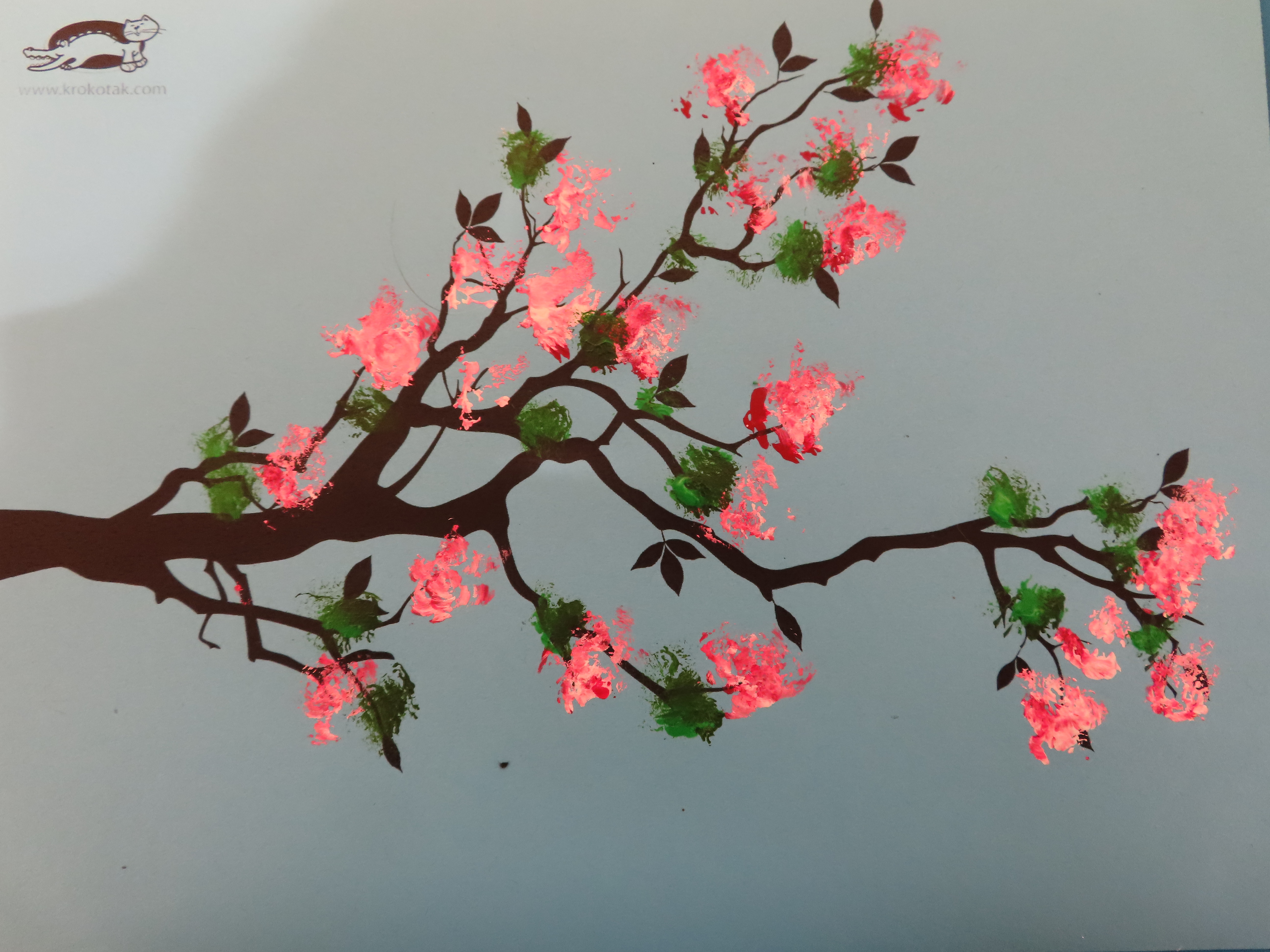 a black tree branch printout with pink and white blossoms and green leaves painted on it