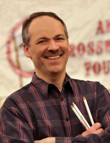 picture of a smiling Will Shortz wearing a plaid shirt and holding 3 pencils