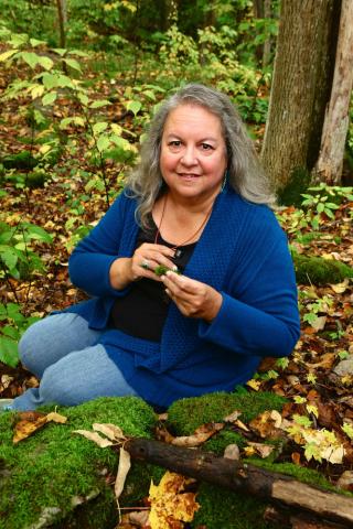 photo of author Robin Wall Kimmerer sitting in the woods