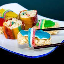 Various candy treats like rice krispies, gummy sharks, and fruit roll ups assembled into shapes resembling traditional sushi rolls.