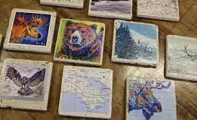 Ceramic coasters of differing sizes each with a different image (moose, bear, map, bird, etc.) affixed to the top.