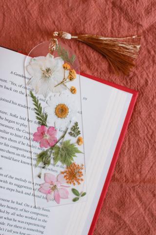 a pressed flower on clear acrylic bookmark on a page of an open book