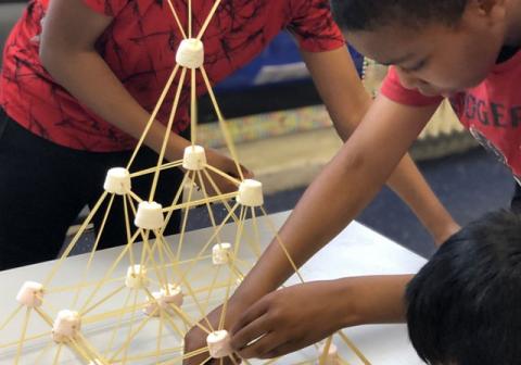 two young men use jumbo marshmallows to create a freestanding tower