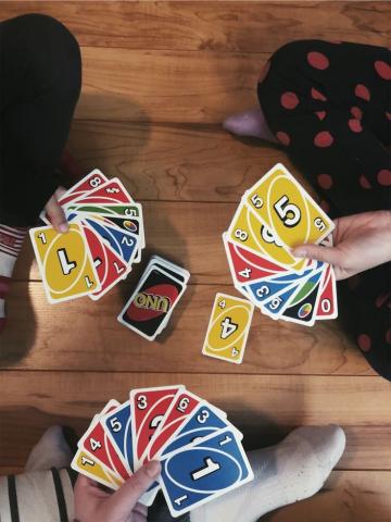 three teens sit cross legged on the floor, each with a handful of Uno cards. A yellow card sits face up in the middle.