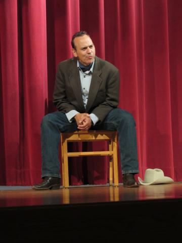 photo of Duffy Hudson portraying Audie Murphy, seated on a stool with a cowboy hat next to him