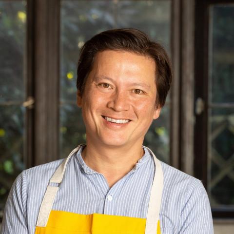 Kenji Lopez-Alt wearing a yellow apron smiles at the camera