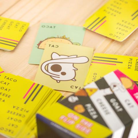brightly colored playing cards for the game Taco Cat Goat Cheese Pizza are strewn about a wooden table