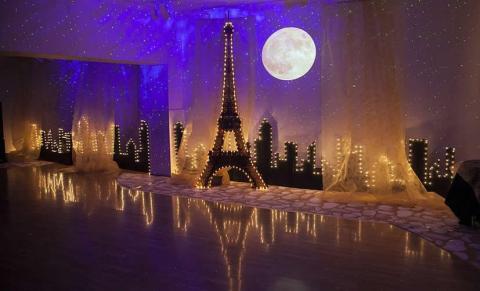 a faux Paris skyline sits against a blue wall. There is a large round moon hanging.