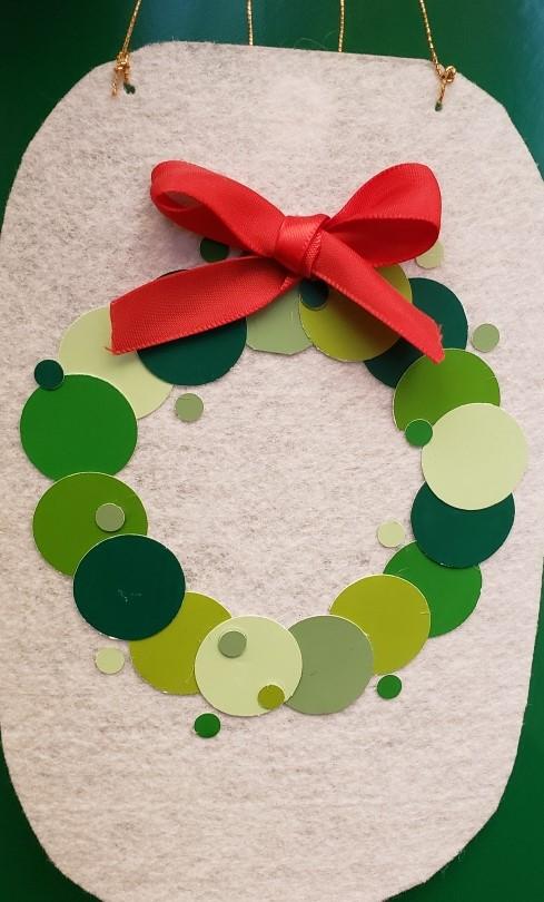 green wreath made of punched out circles on white felt background with red ribbon