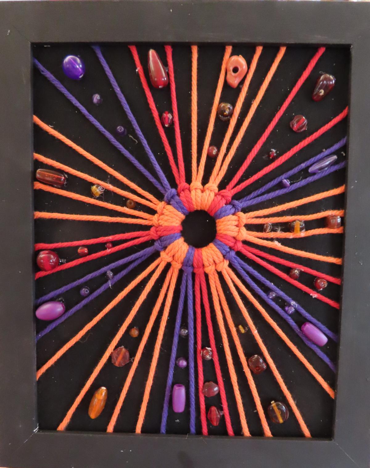  a firework image made of colored yarn within a black frame on a black background