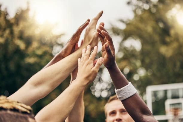 many hands of different ethnicities reach upwards for a group high five