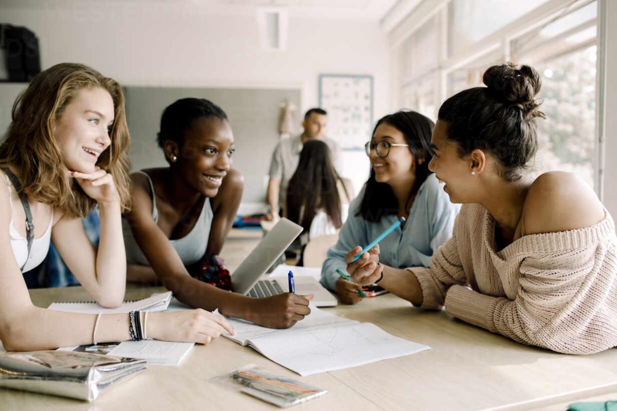 four young women sit around a table, smiling as if sharing ideas